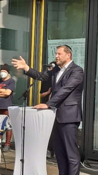 Tim Kurzbach steht erneut am Pult und spricht. Passanten hören zu
